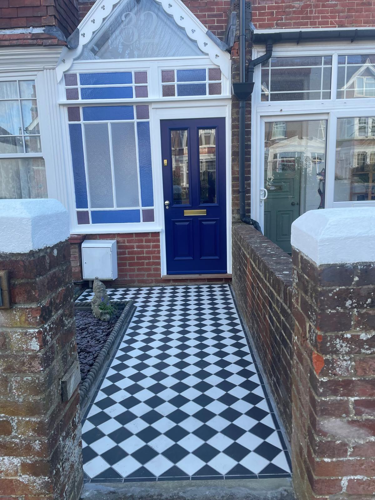 Black and white tiled entrance path between brick walls