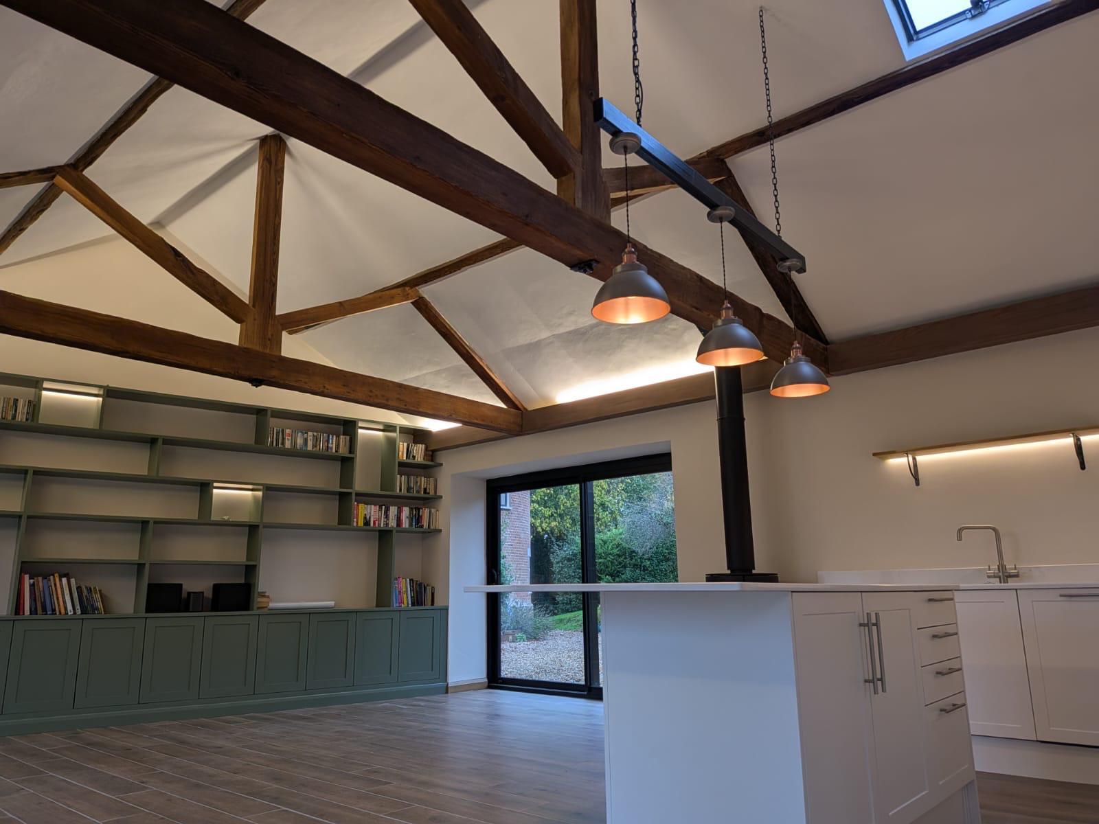 Green fitted kitchen installed around exposed timber roof beams