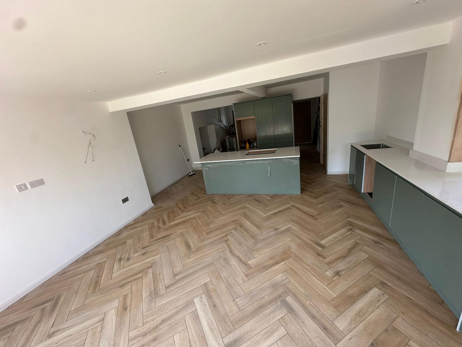 Open-plan kitchen with green cabinetry and herringbone flooring